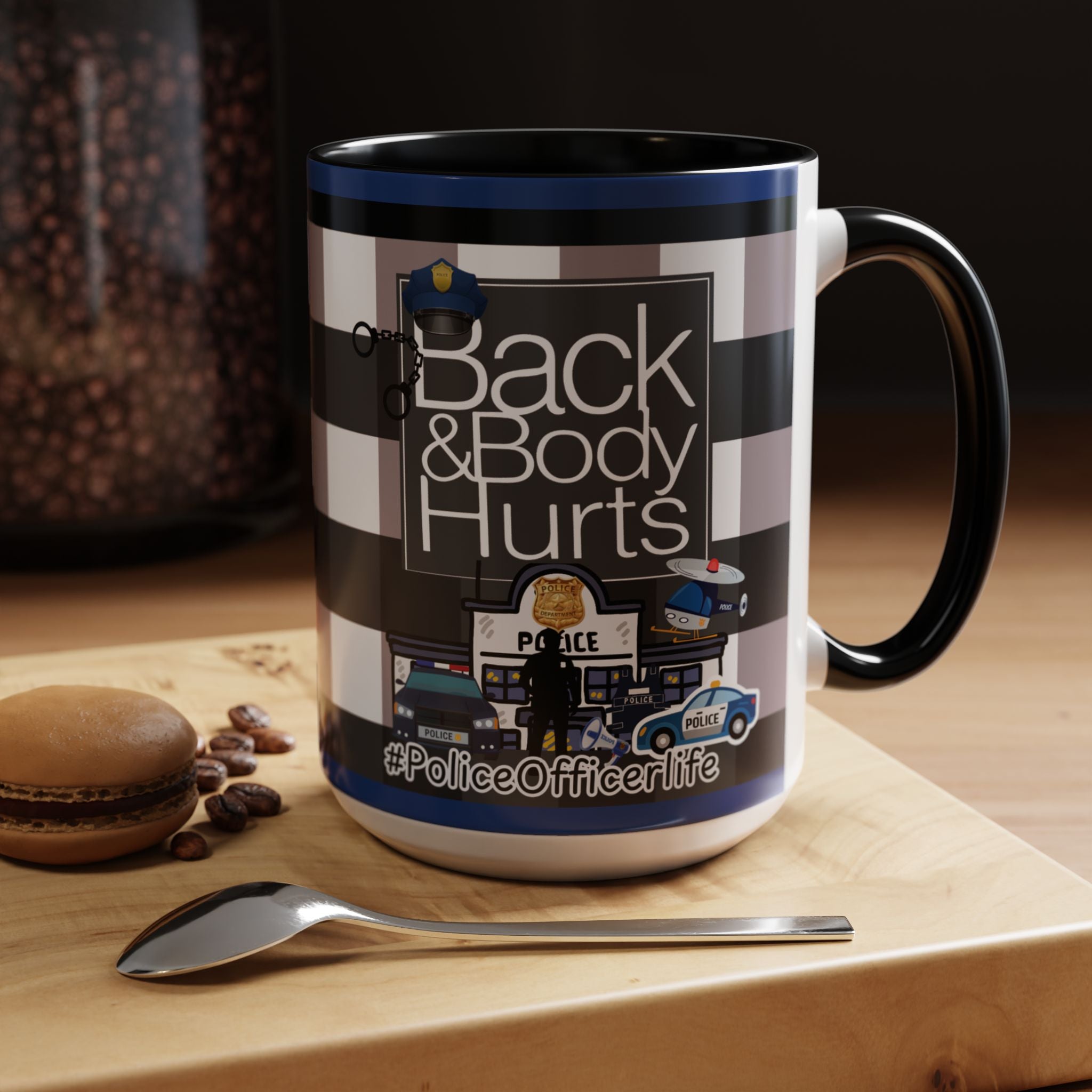 A mug with a design featuring police officers and the text "Back & Body Hurts" on it, placed on a wooden surface next to a spoon.