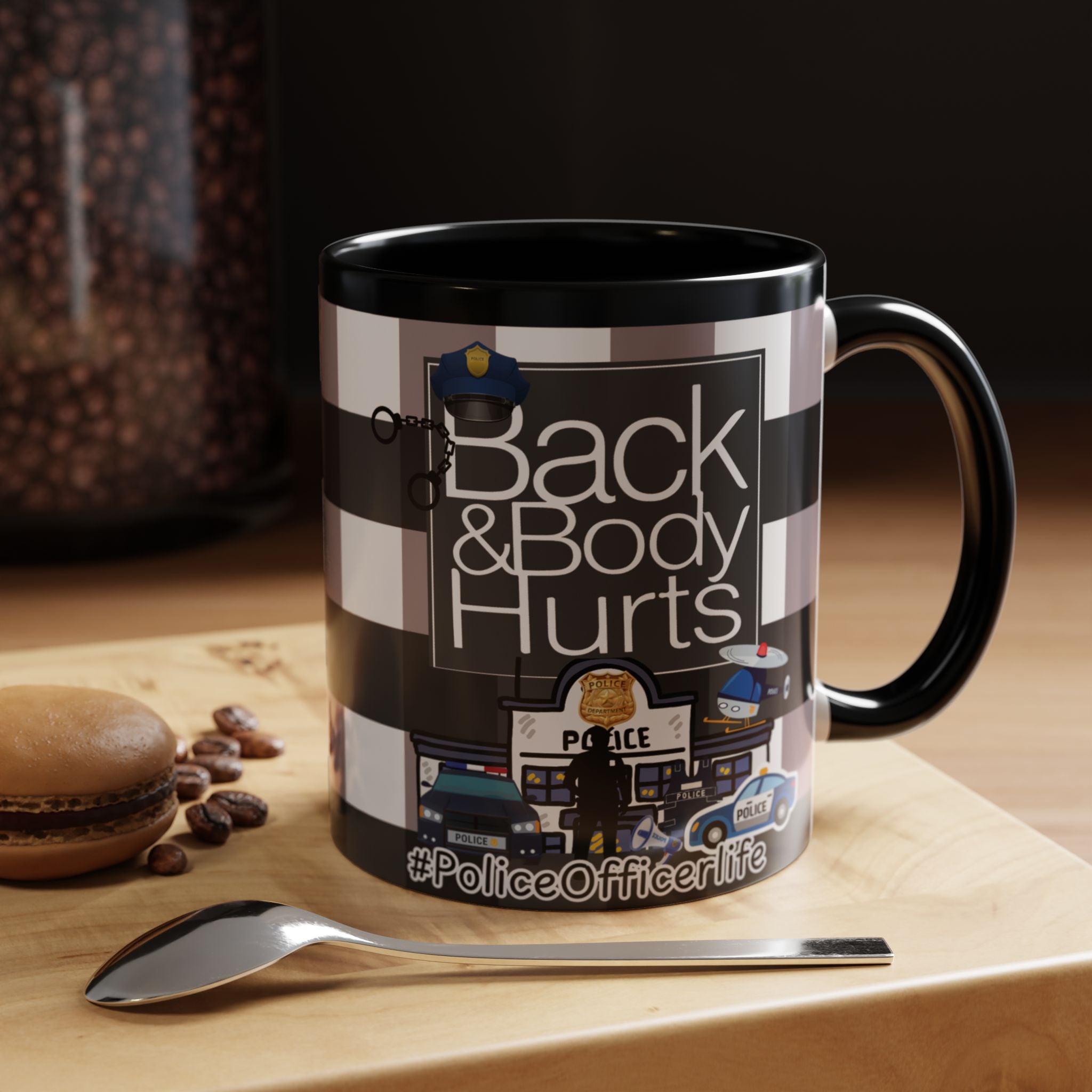 A black and white mug with a graphic design featuring a police officer and the text "Back & Body Hurts" on it, placed on a wooden surface next to a spoon.